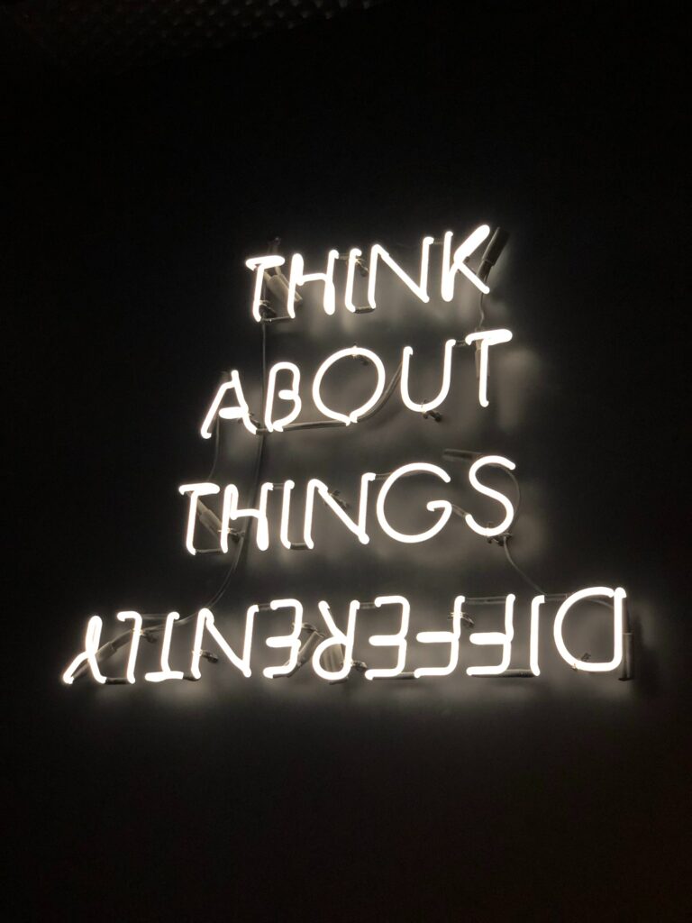 An image with glowing white neon letters, spelling out "Think about things differently." The background is black, making the neon words stand out, and the word differently is spelled upside down.