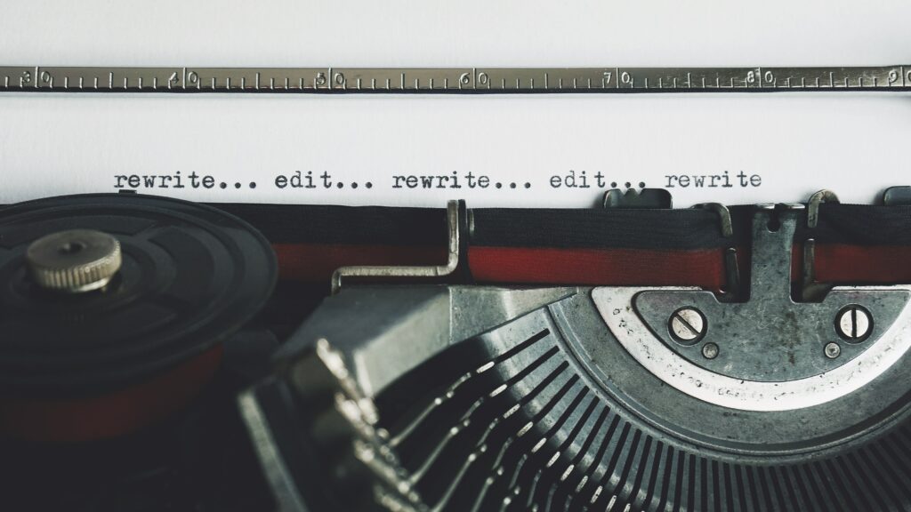 A close-up photograph of a typewriter. There is a sheet of paper in the typewriter, with the text: "rewrite... edit... rewrite... edit... rewrite" in black ink.