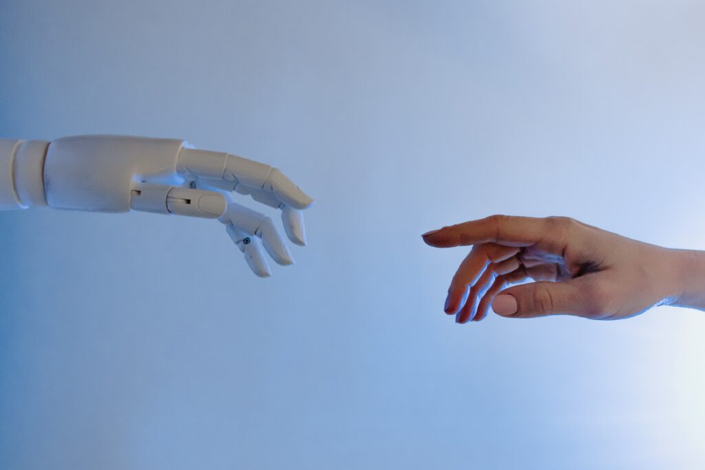 A photograph of a robot and human hand reaching out to touch one another, only inches away. Reminiscent of the "The Creation of Adam" art in the Sistine chapel in Rome.