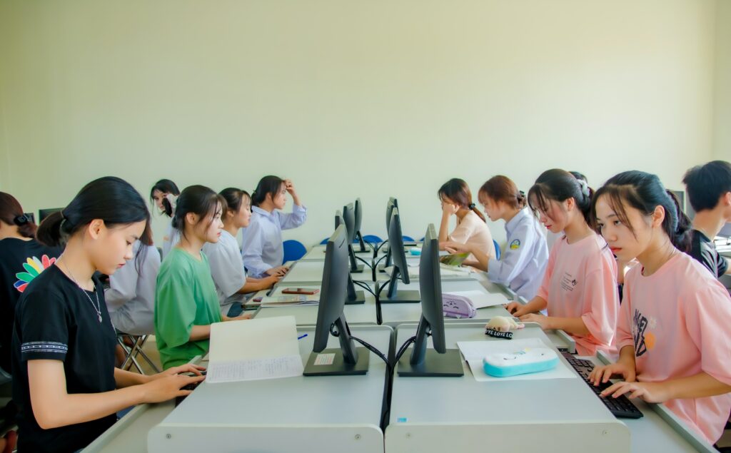 An image of a long line of desks, each with a computer and a student hard a work. The image cuts down the middle of the line of desks, giving a nice, symmetrical look to the photograph. The students appear to be highs chool aged.