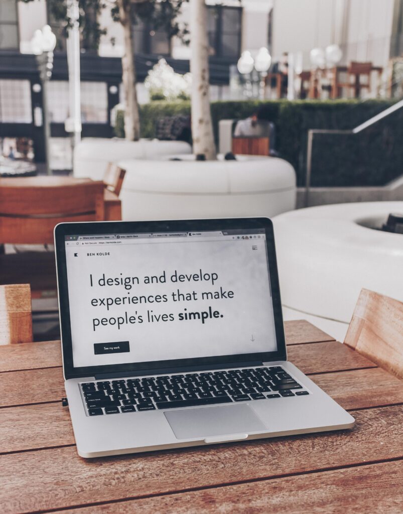 A photograph of an open laptop. The screen on the laptop depicts large black text on a white background, that says "I design and develop experiences that make people's lives simple."