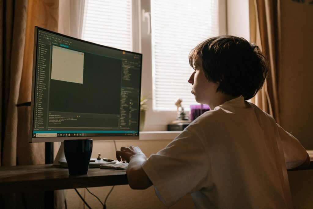 Photograph of a child sitting at a desk, working with a newly opened coding application.